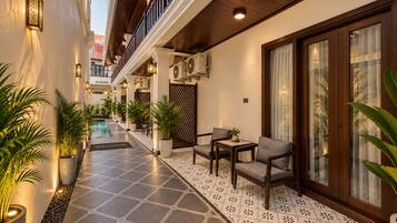 A hotel corridor with a pool, seating area, and potted plants.