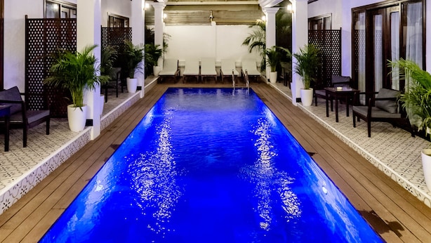 A swimming pool with a wooden deck, white pillars, and outdoor seating. - Cozy An Boutique Hotel Luangprabang (Luang Prabang)