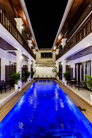 A swimming pool with a wooden deck, white pillars, and outdoor seating. - Cozy An Boutique Hotel Luangprabang (Luang Prabang)