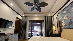 A hotel room with a bed, a desk, a television, a ceiling fan, and a view of the outside balcony. - Cozy An Boutique Hotel Luangprabang (Luang Prabang)