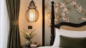 A bedroom with a bed, a nightstand, a vase with flowers, a lamp, and a wall with floral wallpaper.