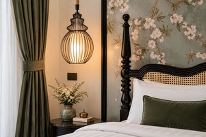 Un dormitorio con cama, mesita de noche, un jarrón con flores, lámpara y papel tapiz con motivos florales.