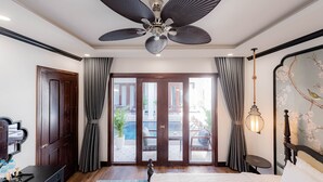 A hotel room with a ceiling fan, a bed, a desk with a coffee machine, a view of the outdoor pool area, and a decorative wall with a floral pattern. - Cozy An Boutique Hotel Luangprabang (Luang Prabang)