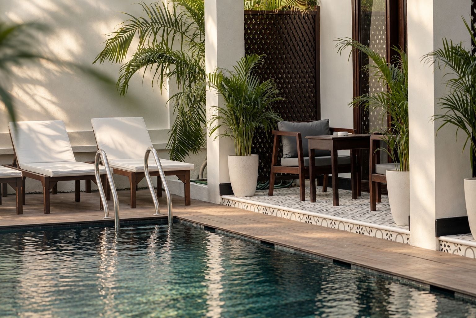 Un área junto a la piscina con sillones, una mesa y plantas en macetas.