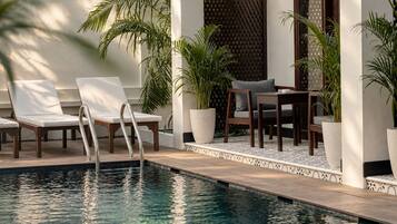 Un área junto a la piscina con sillones, una mesa y plantas en macetas.