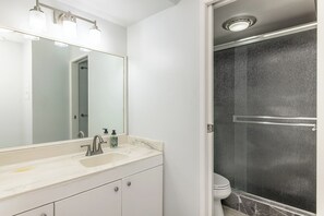 Bathroom features a large mirror, sink, and shower area with a glass door.