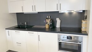 A modern kitchen with white cabinets, a black countertop, and a built-in oven. - "Petit flocon" Apartment in the center of Verbier (Val de Bagnes)