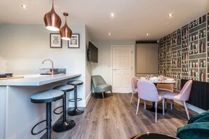 A modern kitchen with a bar area, a dining set, and a bookshelf. - Host & Stay | The Pilgrim Coach House (Liverpool)