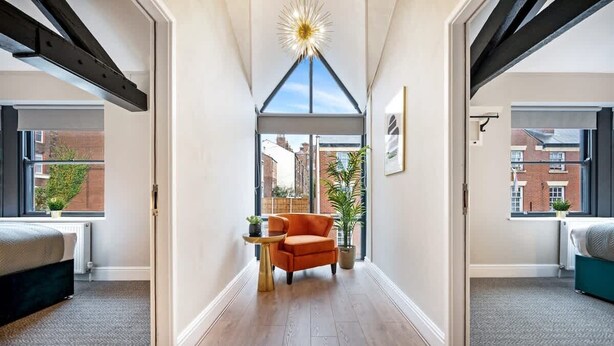 A narrow hallway with a high ceiling, a central seating area with a chair and a small table, and large windows on both sides. - Host & Stay | The Coachouse at Pilgrim St (Liverpool)