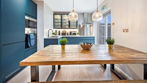 A modern kitchen with blue cabinets, stainless steel appliances, and a wooden dining table with two potted plants. - Host & Stay | The Coachouse at Pilgrim St (Liverpool)