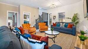 A spacious living area with a sofa, armchairs, and a coffee table. There is a staircase leading to another level. - Host & Stay | The Coachouse at Pilgrim St (Liverpool)