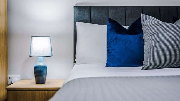 Un lit bien fait, avec une tête de lit, une lampe de chevet et deux oreillers.