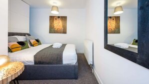 Habitación de hotel con cama, mesita de noche, espejo y un cuadro en la pared.