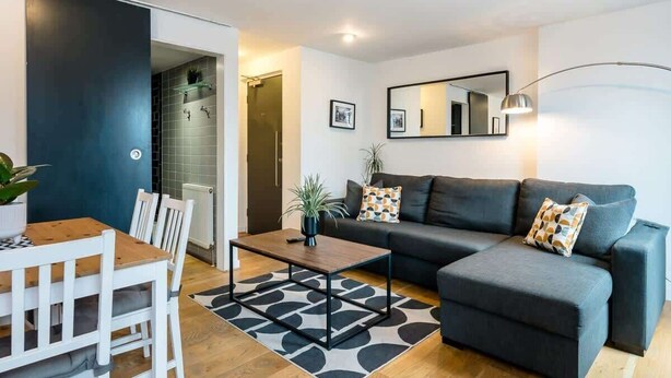 Una sala de estar moderna con un sofá, una mesa de centro, una mesa de comedor con sillas, un tapete con estampado blanco y negro y un espejo grande en la pared.