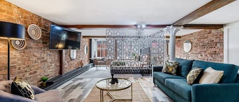 A modern living room with a brick wall, a TV mounted on the wall, a sofa, a coffee table, and a patterned rug.