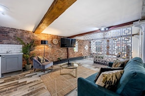 A modern living room with a brick wall, a TV mounted on the wall, a sofa, a coffee table, and a decorative partition. - Host & Stay | Mathew Street Studio (Liverpool)