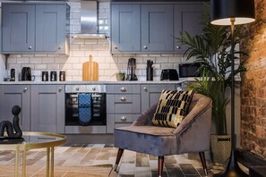 A modern kitchen with grey cabinets, a central island, and a seating area with a chair and lamp. - Host & Stay | Mathew Street Studio (Liverpool)