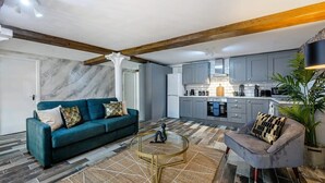 Una sala de estar moderna con sofá, sillón, mesa de centro y una cocina al fondo.