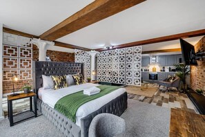 A bedroom with a large bed, a grey armchair, and a wooden side table.