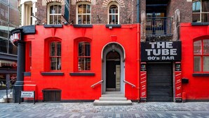 Un edificio rojo con un letrero negro que dice 'THE TUBE 80's BAR'.