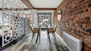 Un comedor con pared de ladrillo, una separadora blanca decorativa y vistas a través de una ventana.