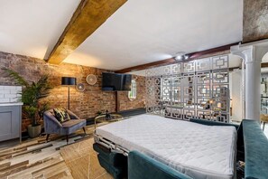 A bedroom with a large bed, a brick wall, a modern TV, and a decorative partition.
