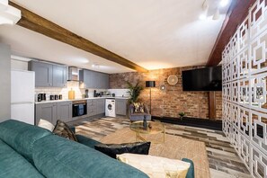 Una cucina moderna con mobili grigi, un forno integrato e una lavatrice. Nell'area soggiorno, un divano verde e un tavolino da caffè.