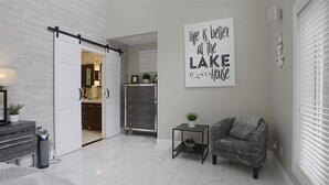 A modern living room with a sliding door leading to a kitchen, a wall-mounted sign, and a patterned armchair.