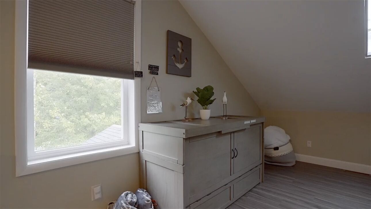 A small, well-lit room with a window, a white cabinet, a potted plant, and a decorative anchor on the wall.
