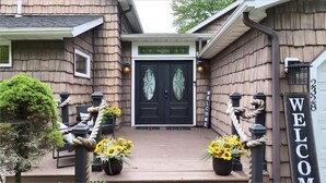 A wooden house with a black double door, a welcome sign, and two potted sunflowers on the porch.