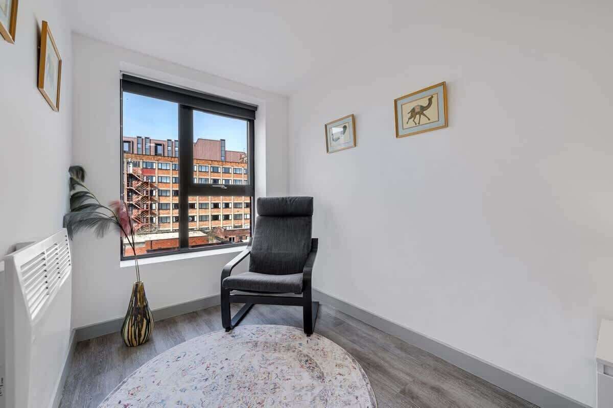 Een moderne kamer met een groot raam, een zwarte stoel, een rond tapijt en twee ingelijste foto's aan de muur.