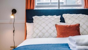 Un lit bien fait, recouvert d’une couvre-lit bleue et blanche, avec deux oreillers blancs à motifs et un seul oreiller marron.