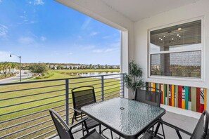 A balcony with a table and chairs, a view of a lake, and a colorful fence. - Beautiful 2BR Condo w/ Private Balcony near Disney (Kissimmee)