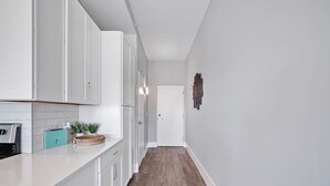 Kapea käytävä, jossa on valkoiset kaapit ja puulattia, ja joka johtaa valkoisiin oviin.