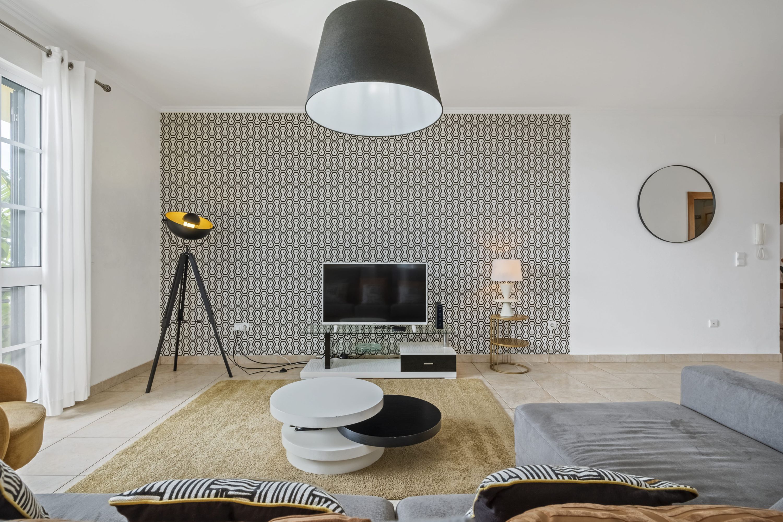 Moderni olohuone, jossa on sohva, sohvapöytä, televisio ja kuviollinen tapetti.