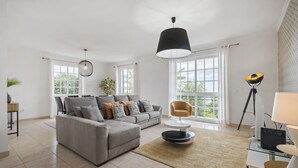 A modern living room with a grey sectional sofa, a round coffee table, and a black pendant light. - Sunny House by Homie (Ponta do Sol)