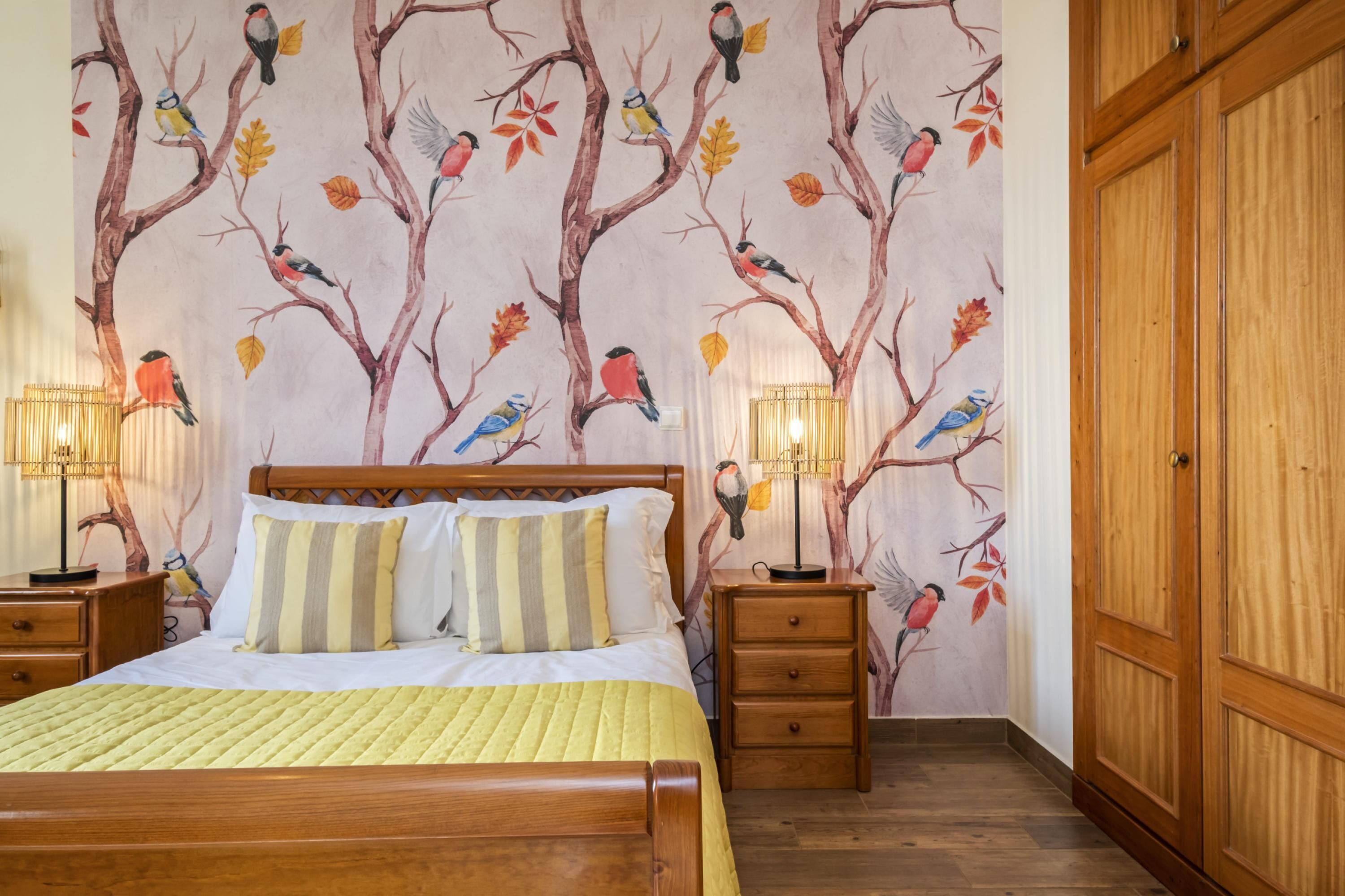 Een net opgemaakt bed met een gestreept kussen, een houten hoofdbord en twee nachtkastjes met lampen.