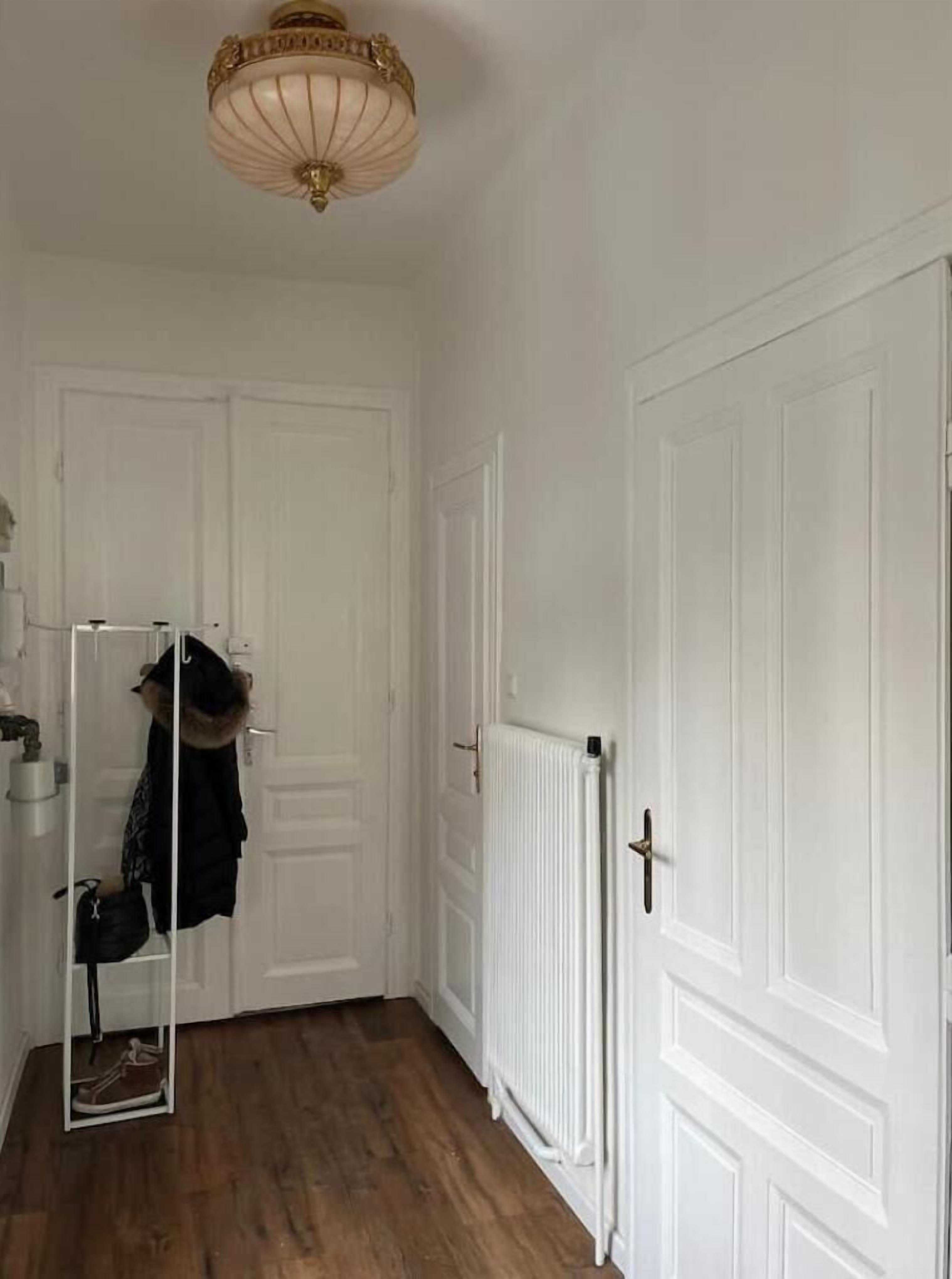 Ein Korridor mit weißen Türen, einem Heizkörper und einem Garderobenschrank mit Fellhut und Jacke.