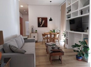 Relax in this stylish living room with a sofa, dining table, and mounted TV.