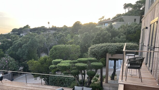 A wooden deck with outdoor furniture, a swimming pool, and a view of a lush, green hillside.