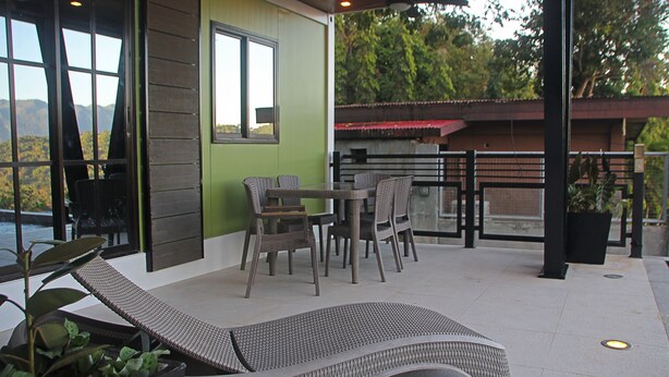 Un espacio de estar techado al aire libre con mobiliario de mimbre, una silla de lounge y vistas a las montañas.