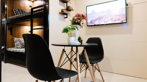 Una habitación con una cama litera, una mesa redonda con dos sillas, una planta en maceta y un televisor en la pared.