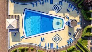 An aerial view of a swimming pool with a geometric tile pattern, surrounded by lounge chairs and a circular seating area. - Holiday Village Apartment With Pool and Garden (San Michele al Tagliamento)