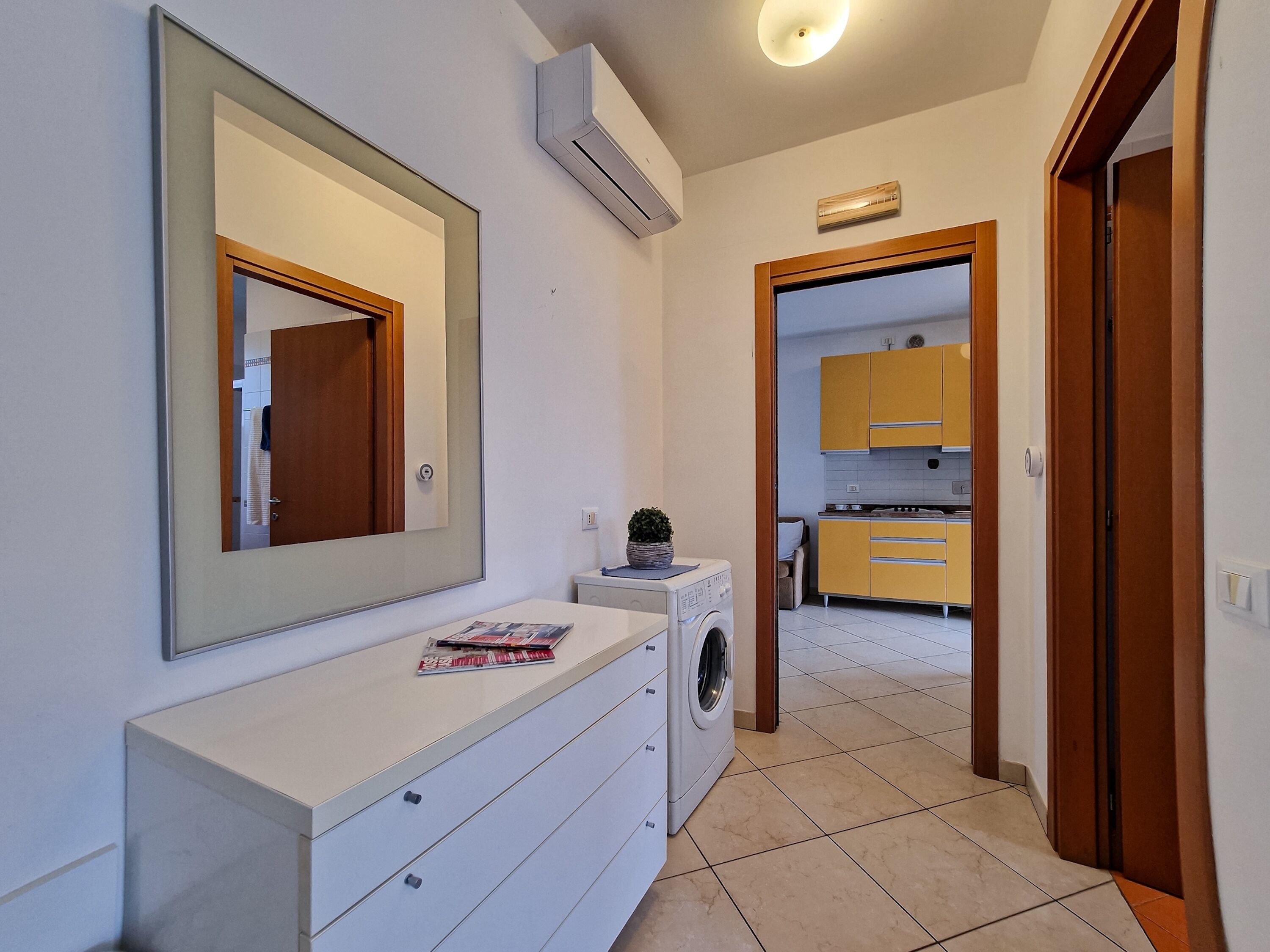 A modern bathroom with a large mirror, a washing machine, and a countertop with a magazine.
