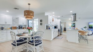 A modern kitchen with white cabinetry, a dining area with wicker chairs, and a central island. - Pet-friendly Cape Coral Gem w/ Pool, 3 Mi to Beach (Cape Coral)