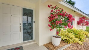 A house with a white door, a potted plant with pink flowers, and a doormat with flamingos. - Pet-friendly Cape Coral Gem w/ Pool, 3 Mi to Beach (Cape Coral)