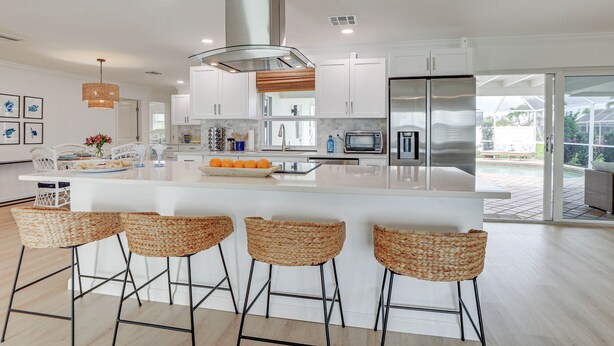 A modern kitchen with white cabinets, a stainless steel range hood, and a large island with bar stools. - Pet-friendly Cape Coral Gem w/ Pool, 3 Mi to Beach (Cape Coral)