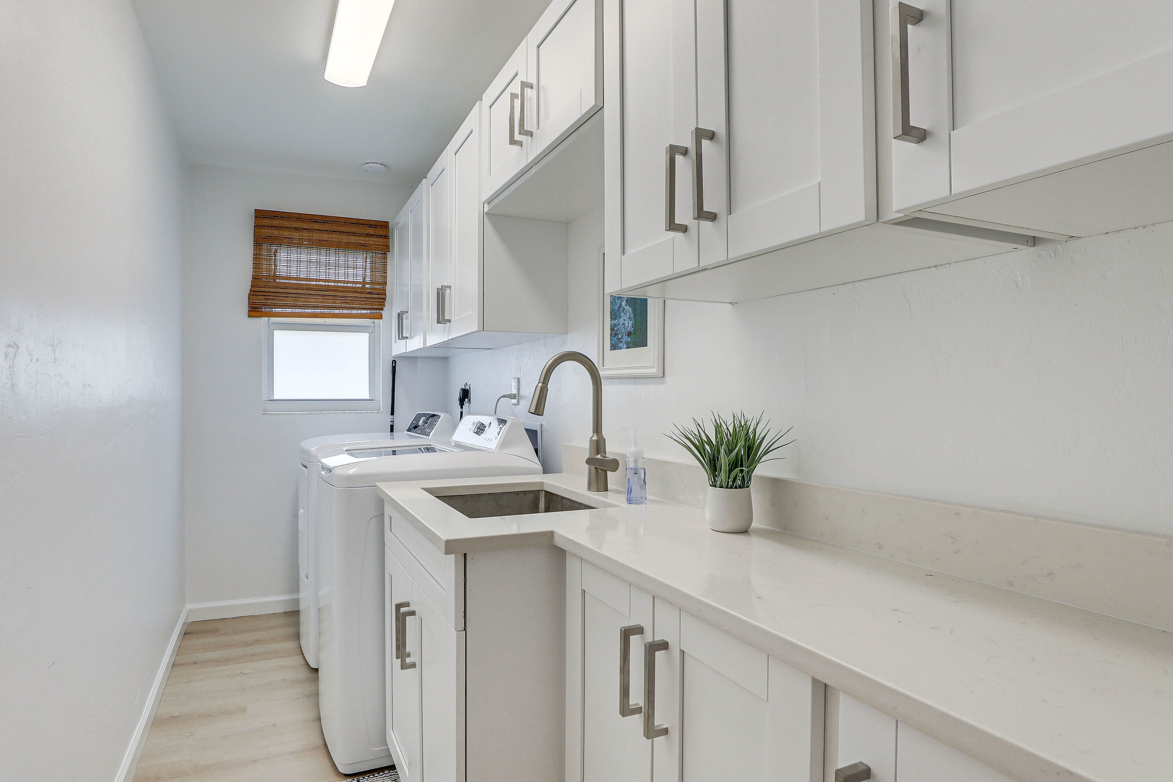 A compact laundry room with a washing machine, a sink, and a window with blinds.