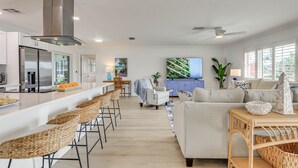 A modern kitchen with a stainless steel range hood, a bar area with wicker chairs, a dining area with a striped chair, and a living room with a sofa and decorative items. - Pet-friendly Cape Coral Gem w/ Pool, 3 Mi to Beach (Cape Coral)