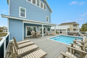 A blue house with a pool, wooden deck chairs, and a covered patio area. - Hangout Vista by GSVR | Roof Deck, Game Room, Theater & Pool | Prime Location + FREE Activities/Golf (Gulf Shores)